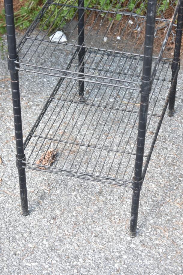 Two black metal shelving units, in used condition, require dismantling before shipping. Buyer responsible for freight costs.