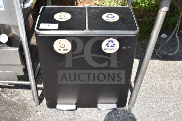 Black dual-compartment trash can with labeled sections for trash and recycling, showing foot pedals and outdoor placement.