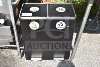 Black dual-compartment trash can with labeled sections for trash and recycling, showing foot pedals and outdoor placement.