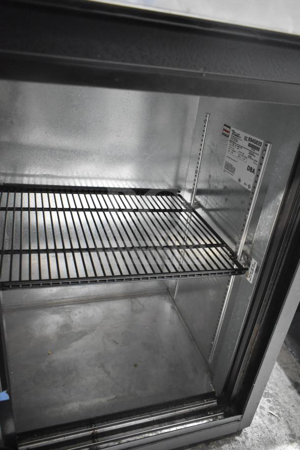 True TBB-24-60G-SD back bar cooler interior. Metal shelving, 115V label. Clean condition, commercial use.