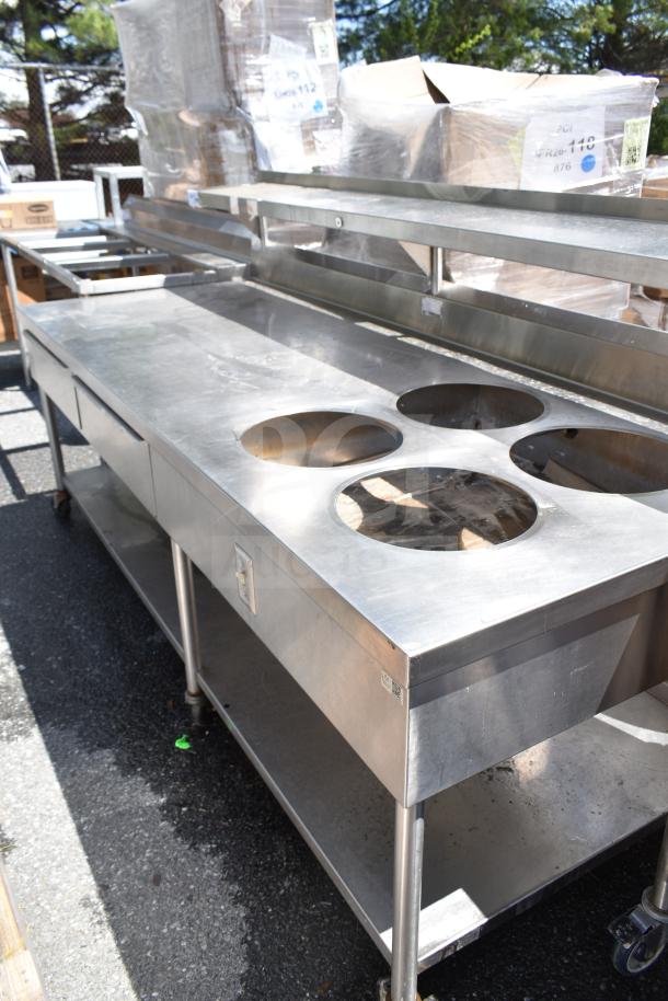 Stainless steel commercial prep table with four round cutouts, two drawers, and sauce pot cutouts on commercial casters.