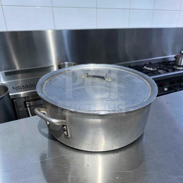 Heavy-duty commercial aluminum stock pot with lid in superior condition on a kitchen counter. Features sturdy handles.
