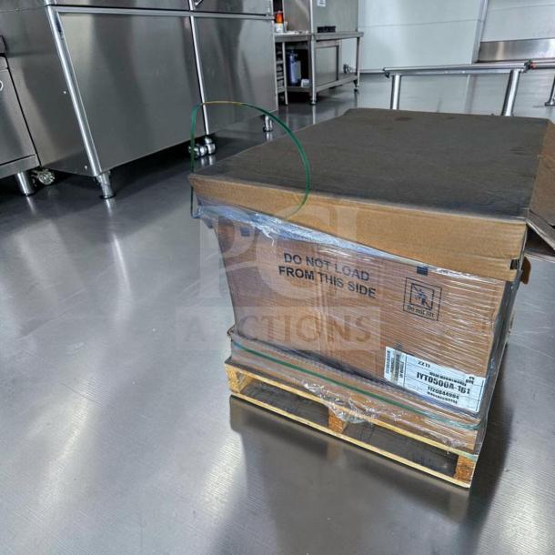 Factory-sealed Manitowoc IYT0500A ice machine in cardboard packaging on pallet, labeled with model and handling instructions.