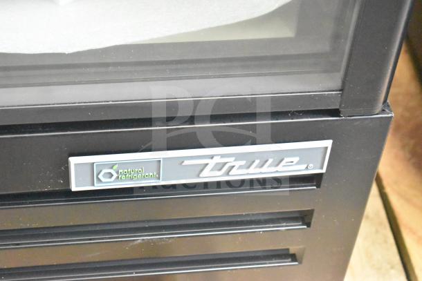 "Close-up of True TVM-36SL-HC cooler, showing brand logo and natural refrigerant label on black exterior."