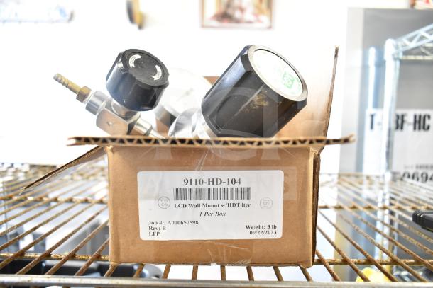Box containing two black-handled gauges, model 9110-HD-104, for LCD wall mount with HD filter. Labels show weight and job details.