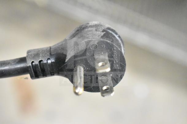 Close-up of a 115V power plug for a 2025 True TVM-48SL-HC commercial cooler. Dust visible on plug surface.