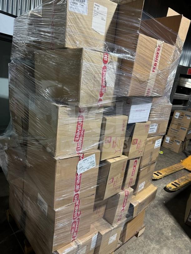 Stacked pallet of assorted boxed items ready for auction, including porcelain bowls, trays, tile, and dispensers.