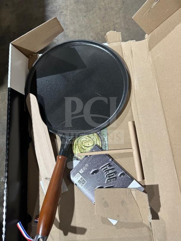 Heavy-duty skillet with wooden handle in open box. Includes a metal stand and care instructions. Appears brand new.