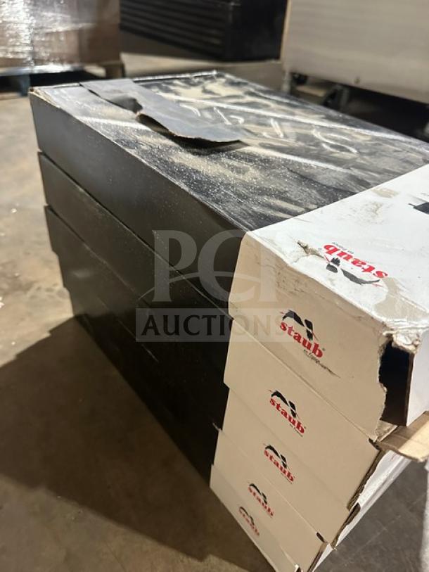 Stack of Staub skillets in boxes, new condition, with Staub branding visible on packaging.