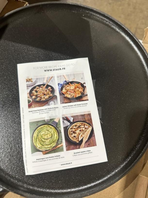 Staub skillet, black cast iron, new condition. Recipe ideas brochure visible on surface. Diameter approx. 10 inches.