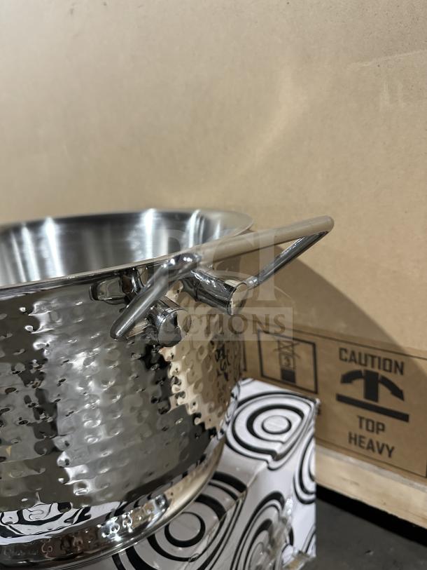 Brand new commercial stainless steel ice bucket with a hammered finish and sturdy handles, shown against box with caution label.
