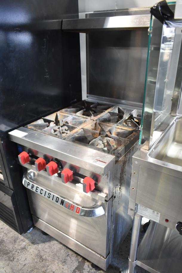 Precision commercial 4-burner gas range with oven, overshelf, backsplash, on casters. Visible wear, red control knobs.