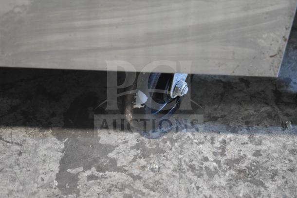 Precision commercial gas range caster, black wheel, attached to stainless steel structure, on worn concrete floor.