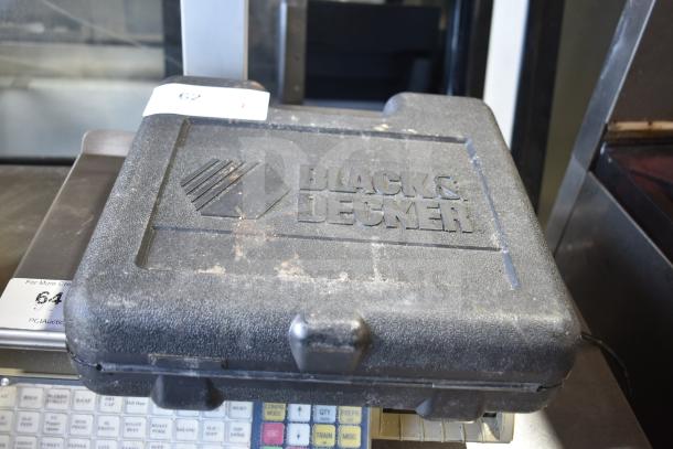 Black & Decker DR220 corded drill in hard case. 120V, 10mm. Case shows wear, logo embossed on top. Auction item label visible.