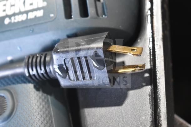 Black & Decker DR220 corded drill plug close-up in hard case, showing 120V, 10mm, with visible wear.
