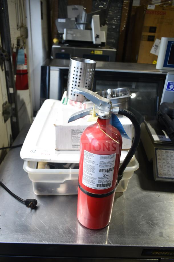 Lot including a red fire extinguisher with labels, stainless steel serving spoons, perforated bin, and various items on a table.