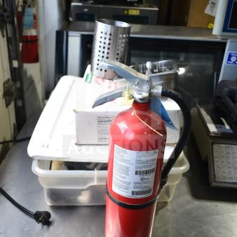 Lot including a red fire extinguisher with labels, stainless steel serving spoons, perforated bin, and various items on a table.