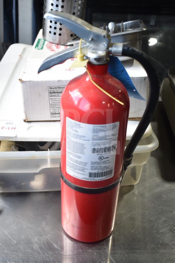 Lot with red fire extinguisher, metal serving spoons, and a plastic bin. Extinguisher has detailed safety labels.