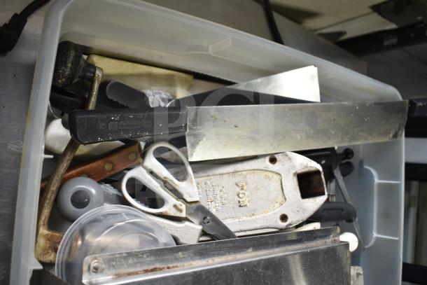Plastic bin filled with various items including a fire extinguisher, serving spoons, knife, and labeled scissors. Mixed condition.
