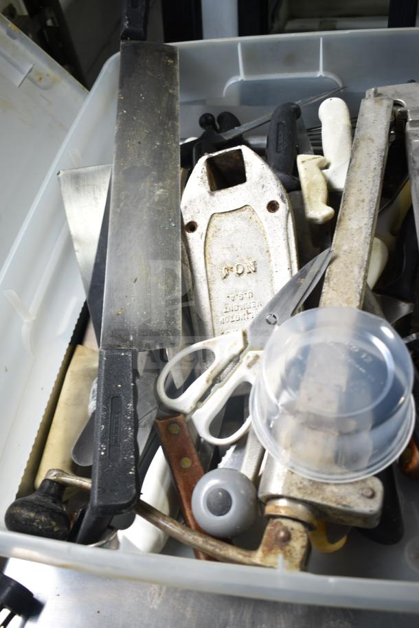 Plastic bin containing various items including a fire extinguisher, serving spoons, scissors, and tools. Some metal items show signs of wear.