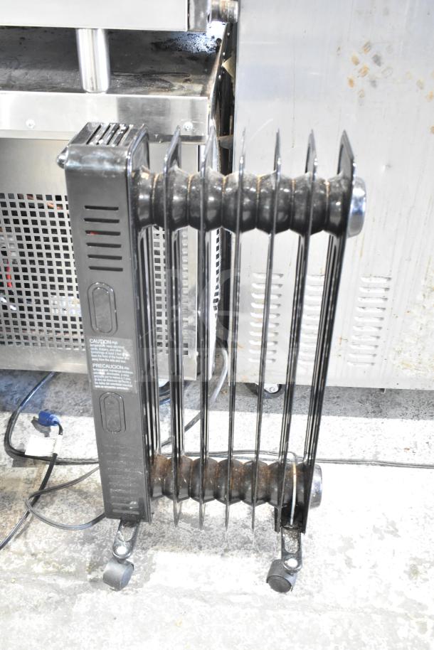 MainStays WSH07O2ABB electric radiator heater, black, vertical fins, visible caution label, on wheeled base.