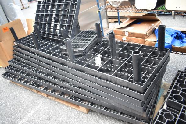 Lot of 7 black poly shelf pieces, stackable, with cylindrical supports. Used condition, arranged on a pallet.