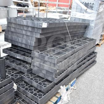 Alt text: Lot of 23 black poly shelf pieces stacked outdoors. Used condition, multiple square compartments per piece, on wooden pallets.