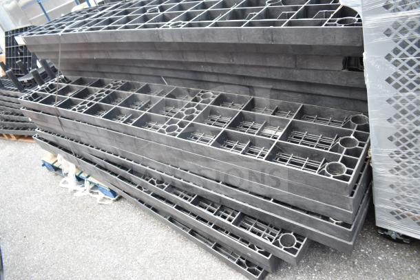 Lot of 23 black poly shelf pieces, stacked outdoors. Durable material, grid design, suitable for shelving projects.