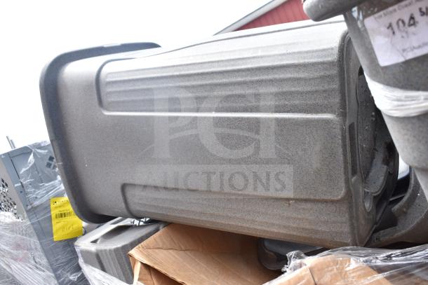 Eight gray plastic trash cans, stacked and wrapped in plastic. Some wear visible. Auction tag present.