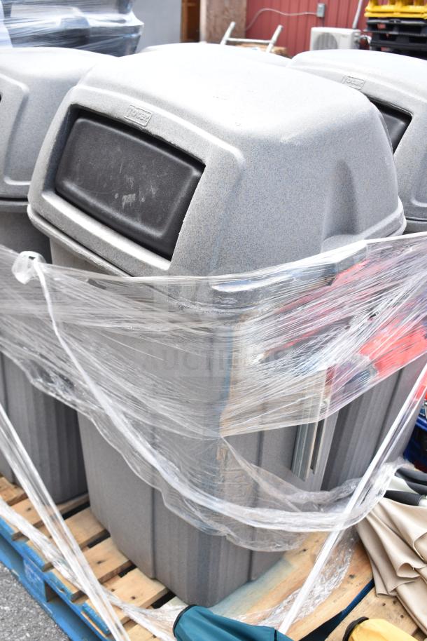 Seven Rubbermaid commercial trash cans, gray, wrapped on a pallet. Durable and ideal for public spaces.