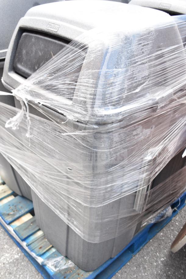 Four gray trash cans wrapped in plastic on a blue pallet. Durable build, ideal for commercial use. Excellent condition.