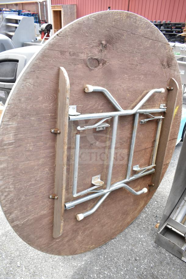 Round folding table, dimensions 58x58x3 inches, wooden top with a metal folding mechanism, in used condition.