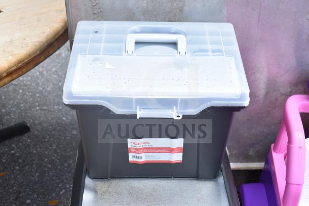 Staples Portable File Tote with clear lid, label indicating storage for hanging files, shown outdoors.