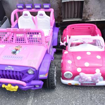 Two children's ride-on vehicles: Disney Princess purple car with two seats, and Minnie Mouse pink car with polka dots.