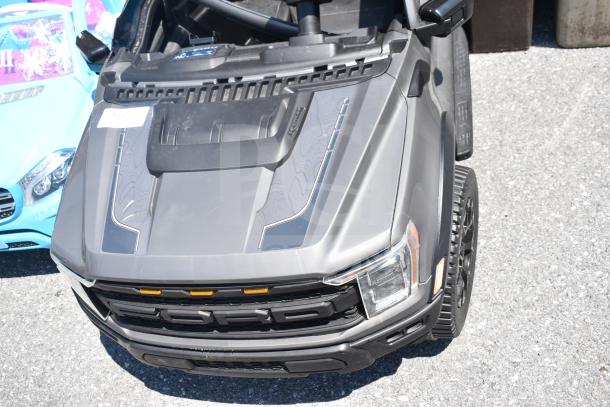 Gray ride-on Ford children's car with black detailing and front lights. Features working steering and rugged tires. Good condition.
