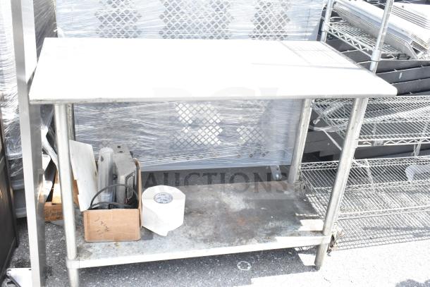 Commercial table with under shelf, metal frame, used condition, visible wear and rust, includes cardboard box and roll.