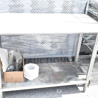 Commercial table with under shelf, metal frame, used condition, visible wear and rust, includes cardboard box and roll.
