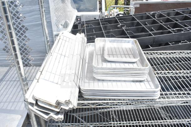 Chrome finish 4-tier wire shelving unit with commercial casters; includes various metal trays, dismantling required for shipping.