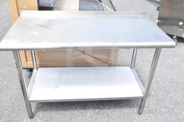 Commercial stainless steel table with under shelf. Used condition with visible wear. Durable workspace for kitchen or workshop.