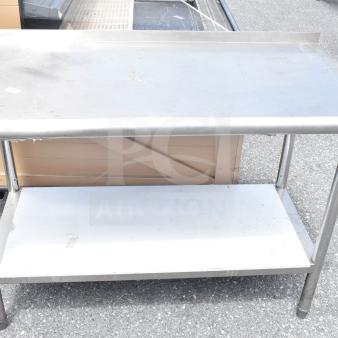 Commercial stainless steel table with under shelf. Used condition with visible wear. Durable workspace for kitchen or workshop.