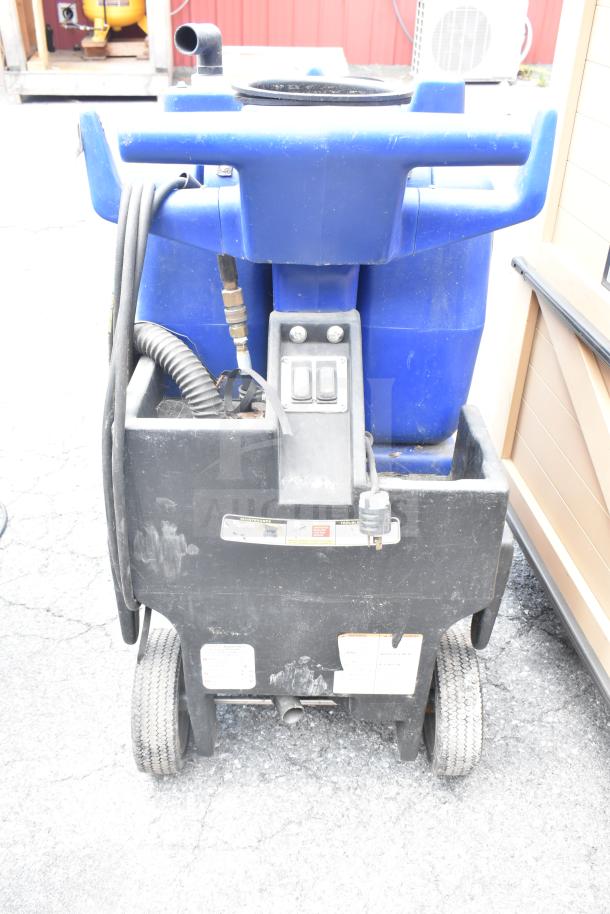 Blue and black floor cleaning machine with wheels, power cord, and controls. Shows wear. Includes instruction labels.