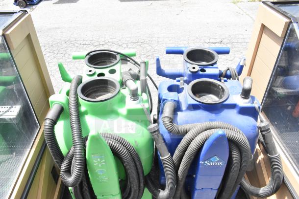 Two floor cleaning machines, one green and one blue, with attached hoses. The green machine is branded with Walmart and labeled "Case Cleaning Cart." The blue machine features a Sam's Club logo. Both appear used.