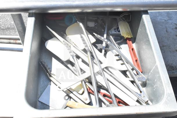 Commercial table with under shelf, two drawers filled with utensils, on commercial casters. Durable metal construction.