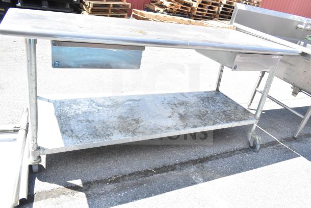 Commercial table with under shelf and two drawers, on commercial casters. Shows surface wear, ideal for industrial use.