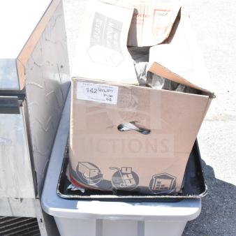 Cardboard box with glasses, mugs, and plates, placed on a plastic bin. Visible item tag marked "142" for auction.