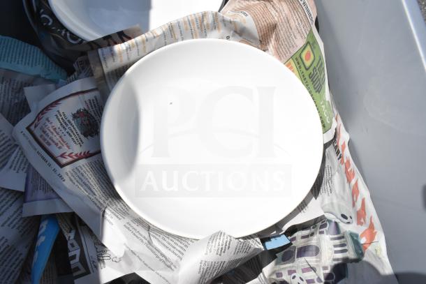 Two boxes with assorted items including white plates and wrapped crockery, on newspaper lining. Auction lot: 2 times your bid.