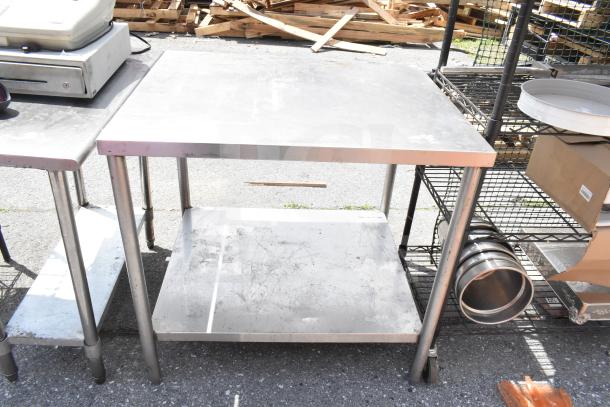 Commercial table with under shelf, stainless steel, sturdy frame, surface wear visible, ideal for kitchen or workshop use.
