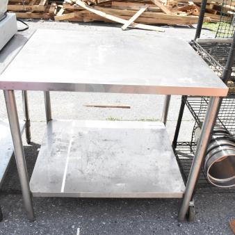 Commercial table with under shelf, stainless steel, sturdy frame, surface wear visible, ideal for kitchen or workshop use.