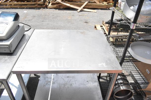 Commercial stainless steel table with under shelf, used condition, visible surface wear, ideal for kitchen or workshop use.