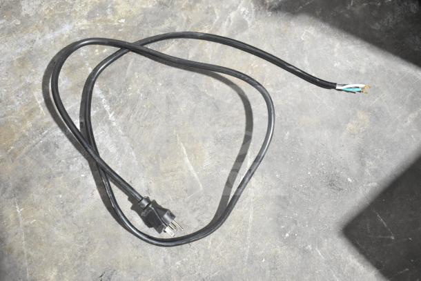 Black power cord with three-prong plug on a concrete surface for Cadco Unox XAFT133-US convection oven.